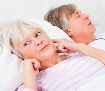 a woman covering her ears beside a snoring man